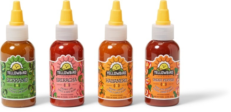 A close-up of the four bottles in the Zesty Organic Hot Sauce Collection, featuring colorful labels and a rustic background.