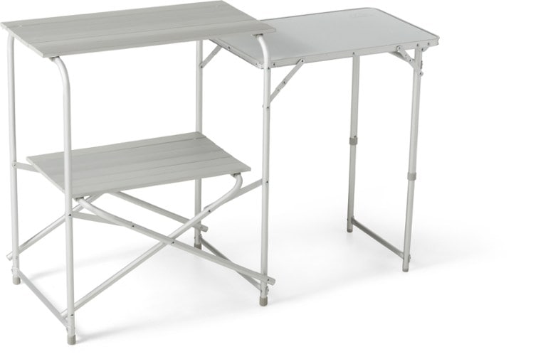 Portable camp kitchen set up at a campsite, featuring adjustable legs and a foldout counter.