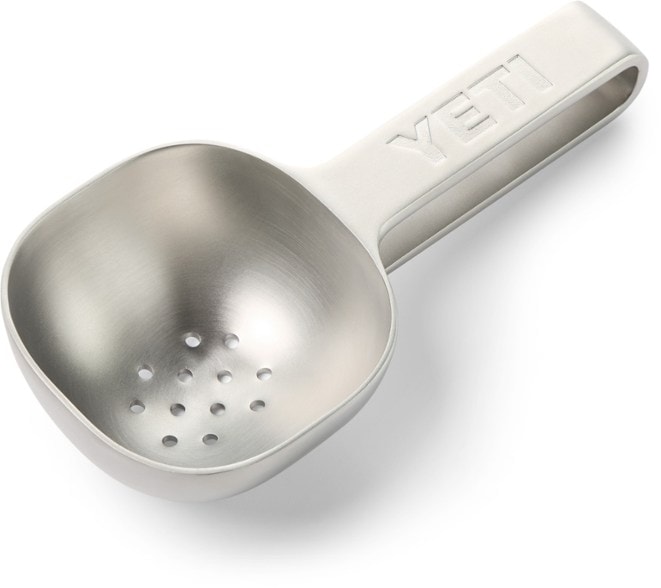 Close-up of ArcticGrip stainless steel scoop with perforated base, resting beside a cocktail shaker.