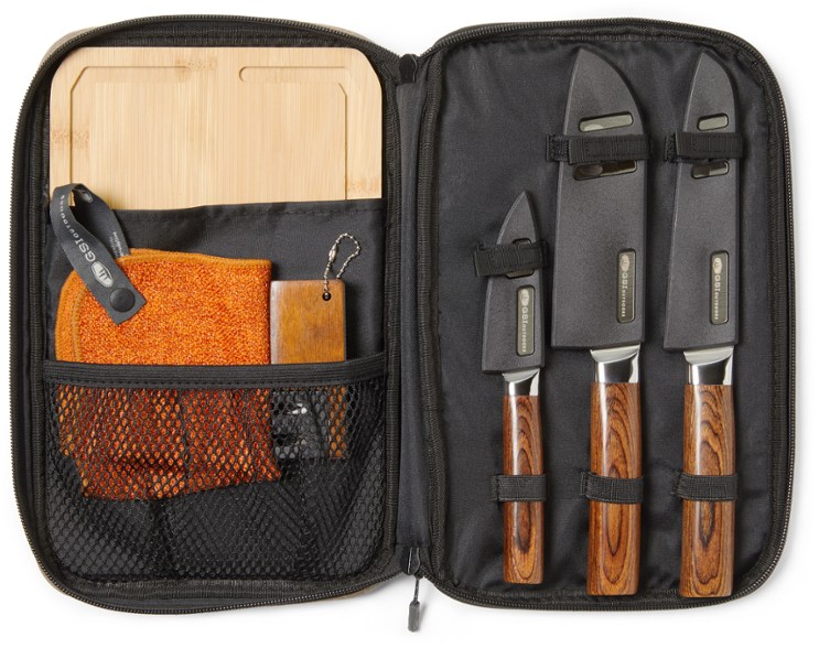 Overhead view of the camping knife set laid out on a picnic table next to fresh vegetables and the bamboo cutting board