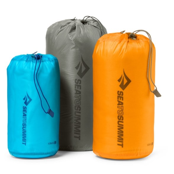 Sea to Summit stuff sacks in grey, blue, and yellow displayed outdoors with backpacking gear