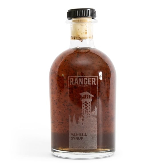 Close-up of vanilla syrup bottle beside a steaming coffee mug—ideal coffee syrup pairing
