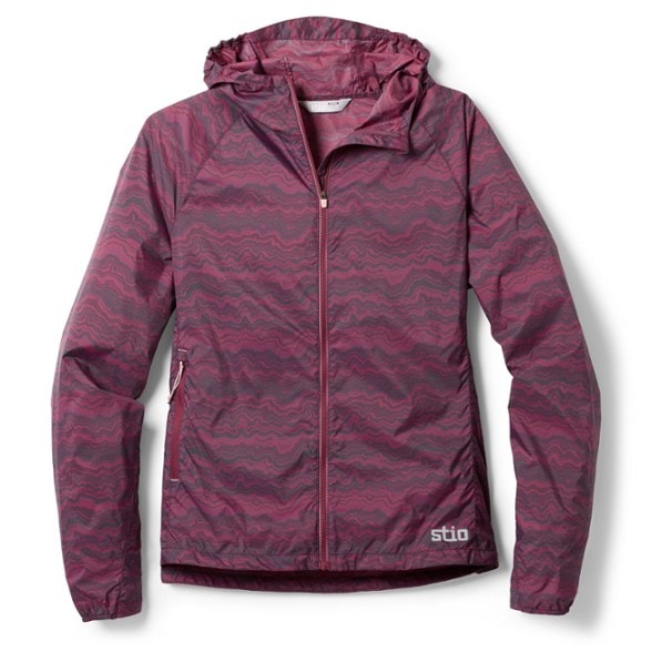 Lightweight women's wind shell showcasing its packable feature in a scenic mountain backdrop.