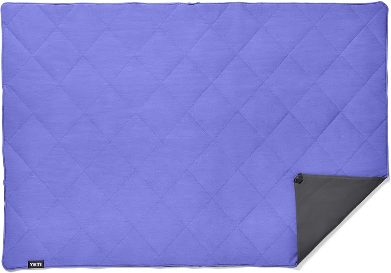 Waterproof camping blanket with padding and insulation laid out on damp forest ground