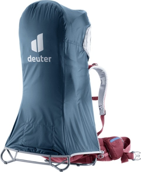 Deuter Kid Comfort Deluxe rain cover on a child carrier in a forest setting.