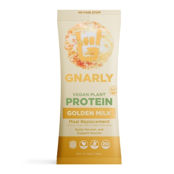 Golden Milk Vegan Protein single serving packet with a warm drink in the background.