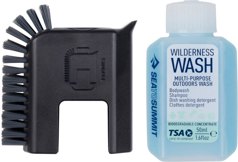 Palm-sized camp scrubber with built-in scraper, photographed beside hiking cookware