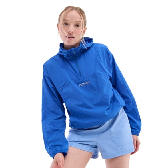 Ultralight women's windbreaker shown in action on a hiking trail, featuring adjustable hood and hem.